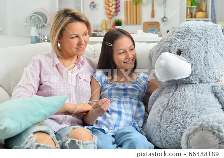 Girl and mother playing with toy teddy bear in facial mask measuring temperature 66388189
