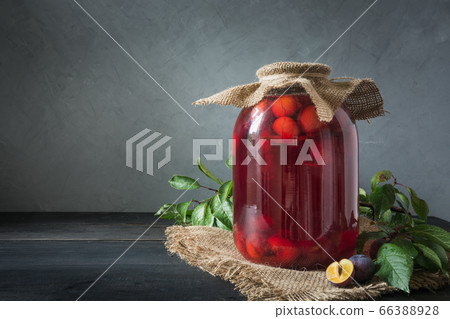 Canned plum compote in large jar on wooden board. Canned plum compote in large jar on wooden board. 66388928