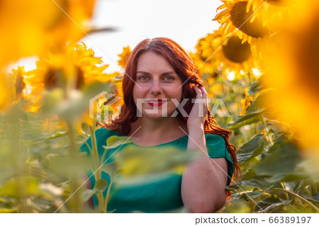Beautiful young girl with long hair in green summer dress in sunflower field at sunset day 66389197