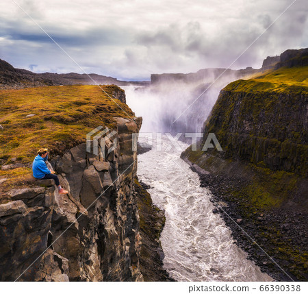 Hiker sitting at the edge of the Gullfoss waterfall in Iceland 66390338