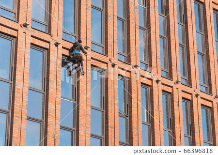 Rope access technician works on highrise building's facade. Rope access technician works on highrise building's facade. 66396818