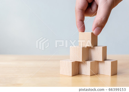 Hand arranging wood block stacking as step stair on top pyramid 66399153