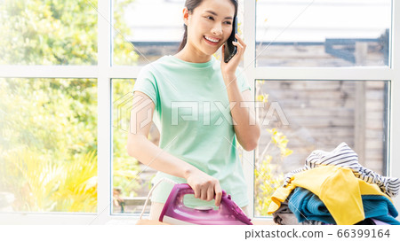 熨燙家務的人材料時的年輕家庭主婦女人手機 熨燙家務的人材料時的年輕家庭主婦女人手機 66399164