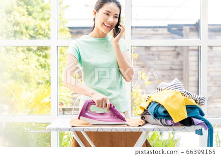 熨燙家務的人材料時的年輕家庭主婦女人手機 熨燙家務的人材料時的年輕家庭主婦女人手機 66399165