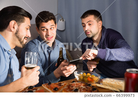 Male friends sitting with phone at home Male friends sitting with phone at home 66399973