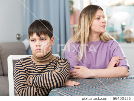 Offended son sitting at tablr after quarrel with mother at home Offended son sitting at tablr after quarrel with mother at home 66400136