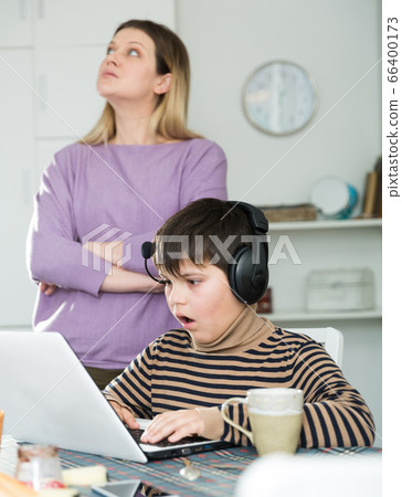 Son plaing video games at laptop, sad mom on background Son plaing video games at laptop, sad mom on background 66400173