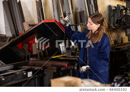 Woman factory worker cuts profile pipe with a band saw Woman factory worker cuts profile pipe with a band saw 66400192