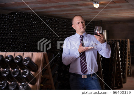 Wine producer inspecting quality of red wine in winery vault Wine producer inspecting quality of red wine in winery vault 66400359