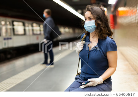 Woman in mask with earphones on subway station 66400617