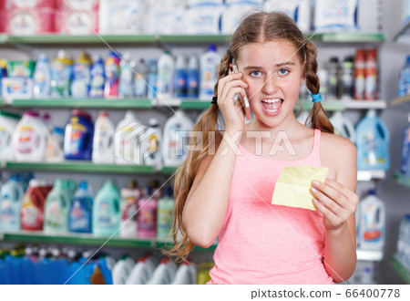 Teenage girl choosing goods with shopping list and talking by phone Teenage girl choosing goods with shopping list and talking by phone 66400778