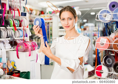 Portrait of delighted young woman with colorful ribbons for sewing in haberdasher shop 66400860