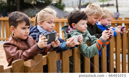 Kids playing with smartphones near wooden fence 66401053