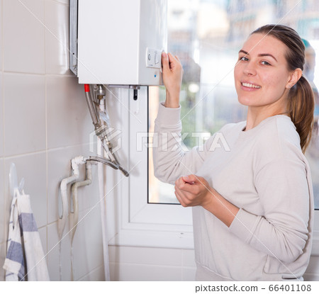 Housewife is standing near gas column and controling temperature of water 66401108
