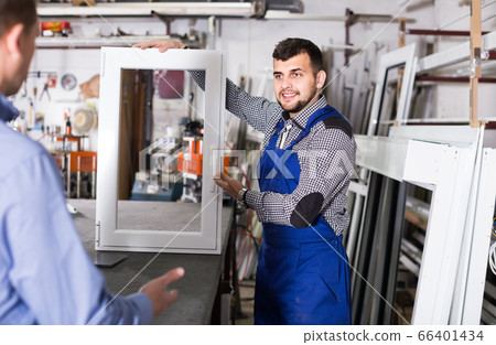 Production worker in coverall demonstrating different PVC windows to customer 66401434