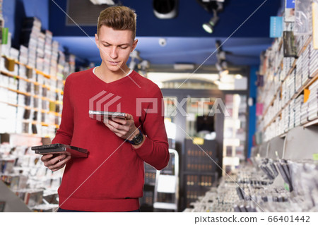 Guy looking CD and DVD in shop attentively reading contents Guy looking CD and DVD in shop attentively reading contents 66401442