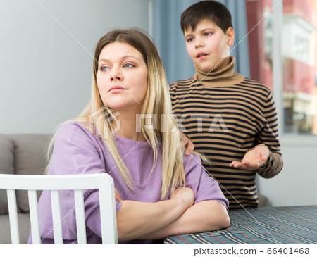 Upset mother sitting at table after arguing with son indoors Upset mother sitting at table after arguing with son indoors 66401468