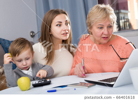 Aged woman is mastering technology near laptop with her daughter and grandson 66401618