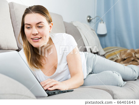 Smiling woman is working with laptop lying on sofa Smiling woman is working with laptop lying on sofa 66401643