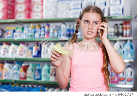 Girl looking goods with shopping list and talking by smartphone Girl looking goods with shopping list and talking by smartphone 66401734