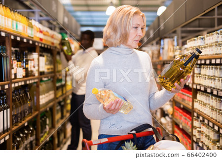 Portrait of thoughtful mature woman looking for vegetable oil in grocery shop Portrait of thoughtful mature woman looking for vegetable oil in grocery shop 66402400