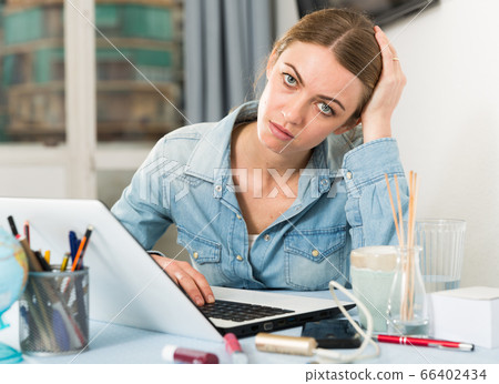 Sad girl looking tired with laptop at table in home interior Sad girl looking tired with laptop at table in home interior 66402434