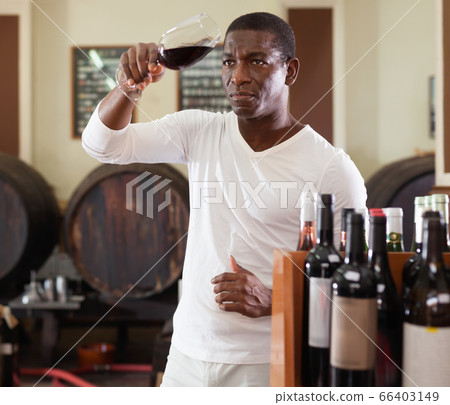 Confident african american male winemaker inspecting quality of red wine, checking it in wine store 66403149