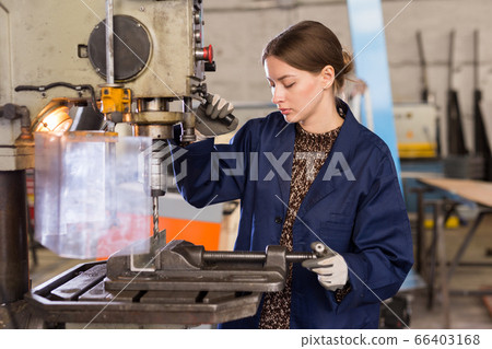 Confident woman mechanic using drilling machine in workshop 66403168
