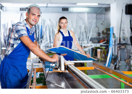 Worker in protective face shield near to circular saw in workshop 66403373