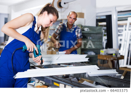 Young workwoman is assembling metal-plastic window using electric drill. Young workwoman is assembling metal-plastic window using electric drill. 66403375