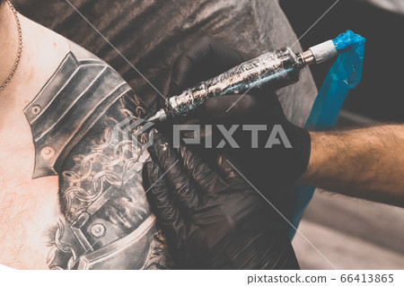 Tattoo salon. The tattoo master is tattooing a man on his shoulder. Tattoo machine, safety and hygiene at work. Close-up, tinted, tattooist Tattoo salon. The tattoo master is tattooing a man on his shoulder. Tattoo machine, safety and hygiene at work. Close-up, tinted, tattooist 66413865