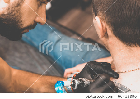 Tattoo salon. The tattoo master is tattooing a man on his shoulder. Tattoo machine, safety and hygiene at work. Close-up, tinted, tattooist Tattoo salon. The tattoo master is tattooing a man on his shoulder. Tattoo machine, safety and hygiene at work. Close-up, tinted, tattooist 66413890