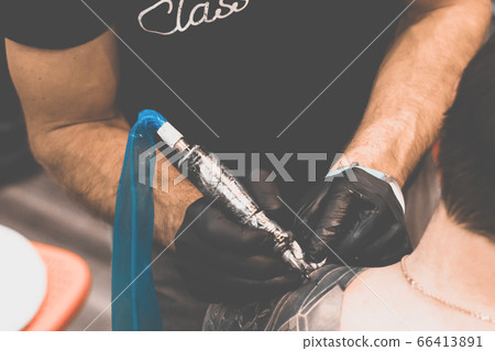 Tattoo salon. The tattoo master is tattooing a man on his shoulder. Tattoo machine, safety and hygiene at work. Close-up, tinted, tattooist Tattoo salon. The tattoo master is tattooing a man on his shoulder. Tattoo machine, safety and hygiene at work. Close-up, tinted, tattooist 66413891