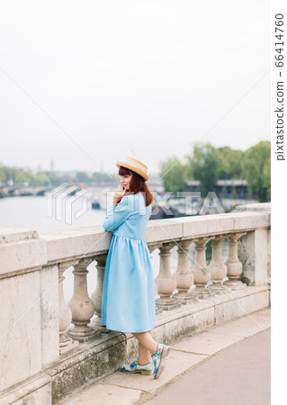 Young attractive woman in blue dress and straw hat, enjoying great view on the Paris and Seine river, standing on the bridge and looking away 66414760