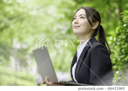 操作計算機的年輕女商人在新鮮的綠樹背景下 操作計算機的年輕女商人在新鮮的綠樹背景下 66415965