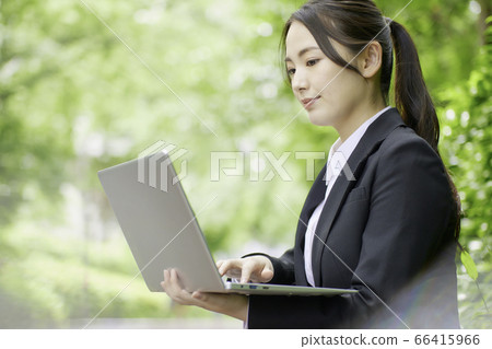 操作計算機的年輕女商人在新鮮的綠樹背景下 操作計算機的年輕女商人在新鮮的綠樹背景下 66415966