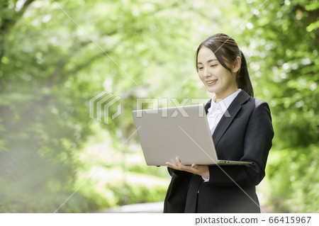 操作計算機的年輕女商人在新鮮的綠樹背景下 操作計算機的年輕女商人在新鮮的綠樹背景下 66415967