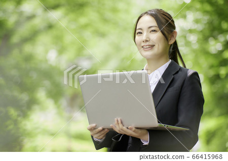 操作計算機的年輕女商人在新鮮的綠樹背景下 操作計算機的年輕女商人在新鮮的綠樹背景下 66415968