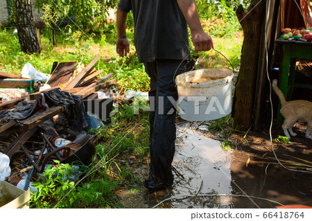 A man carries a white bucket of water to water the 66418764