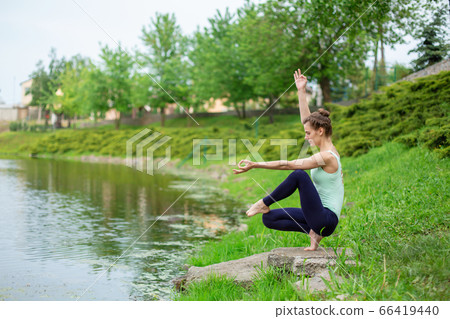 A young sports girl practices yoga on a green lawn A young sports girl practices yoga on a green lawn 66419440