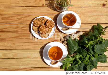 Alternative tea with linden in white cup of tea and cookies with wooden spoons on a brown wooden background. Healthcare tea, alternative medcine Alternative tea with linden in white cup of tea and cookies with wooden spoons on a brown wooden background. Healthcare tea, alternative medcine 66425291