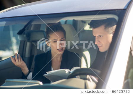 Man at wheel looking at documents and reasoning woman nearby 66425723