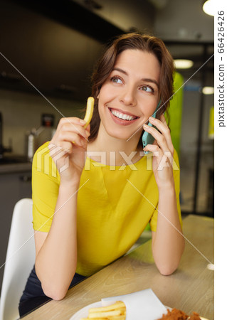 Cute smiling woman holding french fries talking with smartphone 66426426