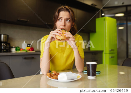 Dark-haired girl biting off a burger looking to the side Dark-haired girl biting off a burger looking to the side 66426429
