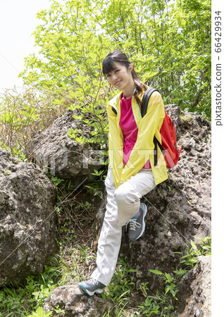 Woman posing sitting on a large rock in a forest surrounded by greenery Woman posing sitting on a large rock in a forest surrounded by greenery 66429934