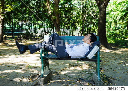 Asian businessman is lying on bench. 66430473