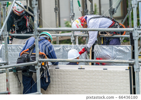 Male worker assembling a prefabricated house in the rain Male worker assembling a prefabricated house in the rain 66436180