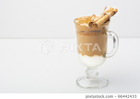 Dalgona Coffee Iced, a Korean fashionable whipped black instant coffee with milk, on a white background. On a glass of cinnamon sticks and chocolate chips. Copy space. Direct view. 66442433