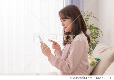 年輕女子坐在沙發上,看著智能手機 年輕女子坐在沙發上,看著智能手機 66442904