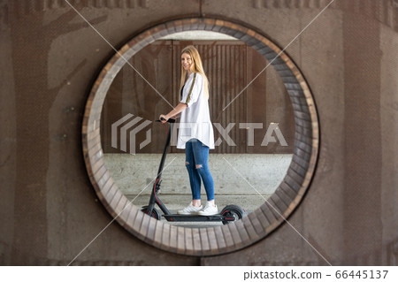 Casual caucasian teenager riding urban electric scooter in urban environment. Urban mobility concept 66445137